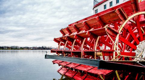 Red and white paddlewheeler docked on the rivers edge.