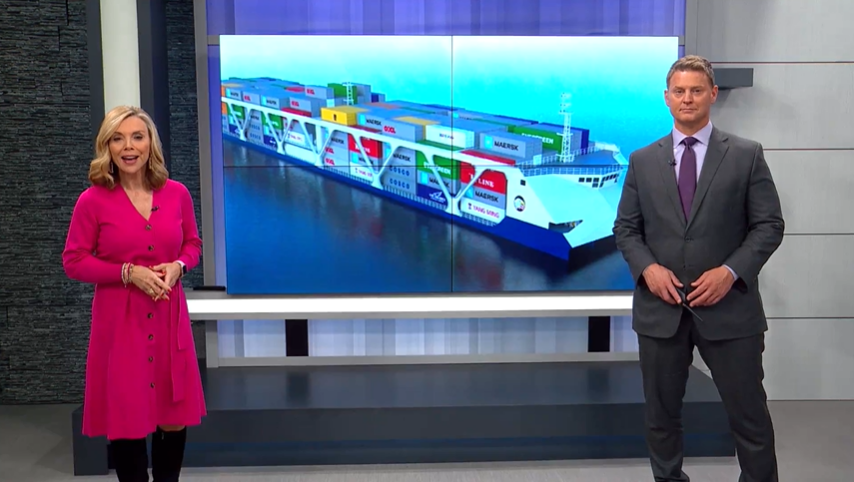 News anchors from Fox 2 report on a potential solution to our nation's supply chain woes in front of a background of a ferry loaded with cargo containers.
