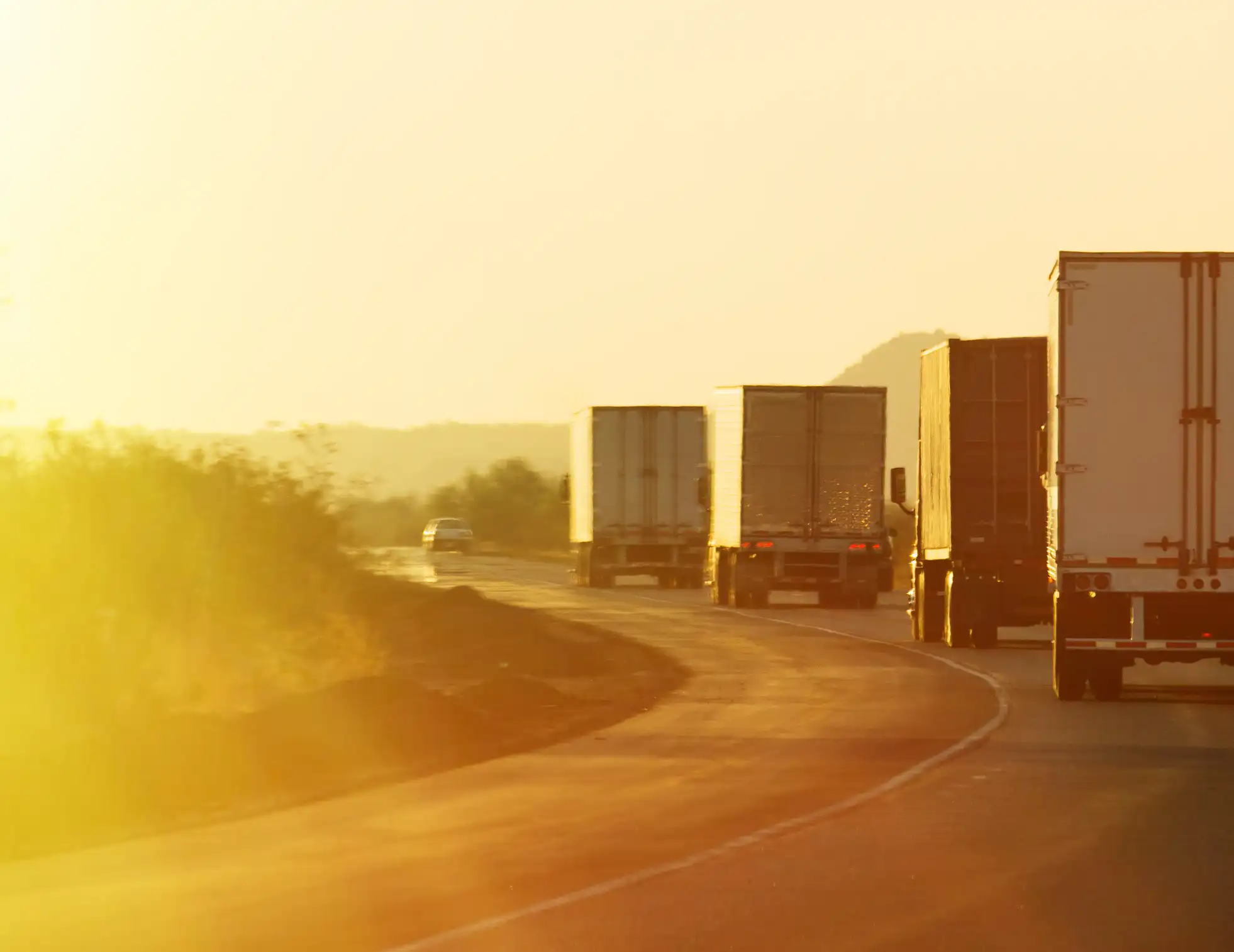 A line of semi trucks driving at sunset.